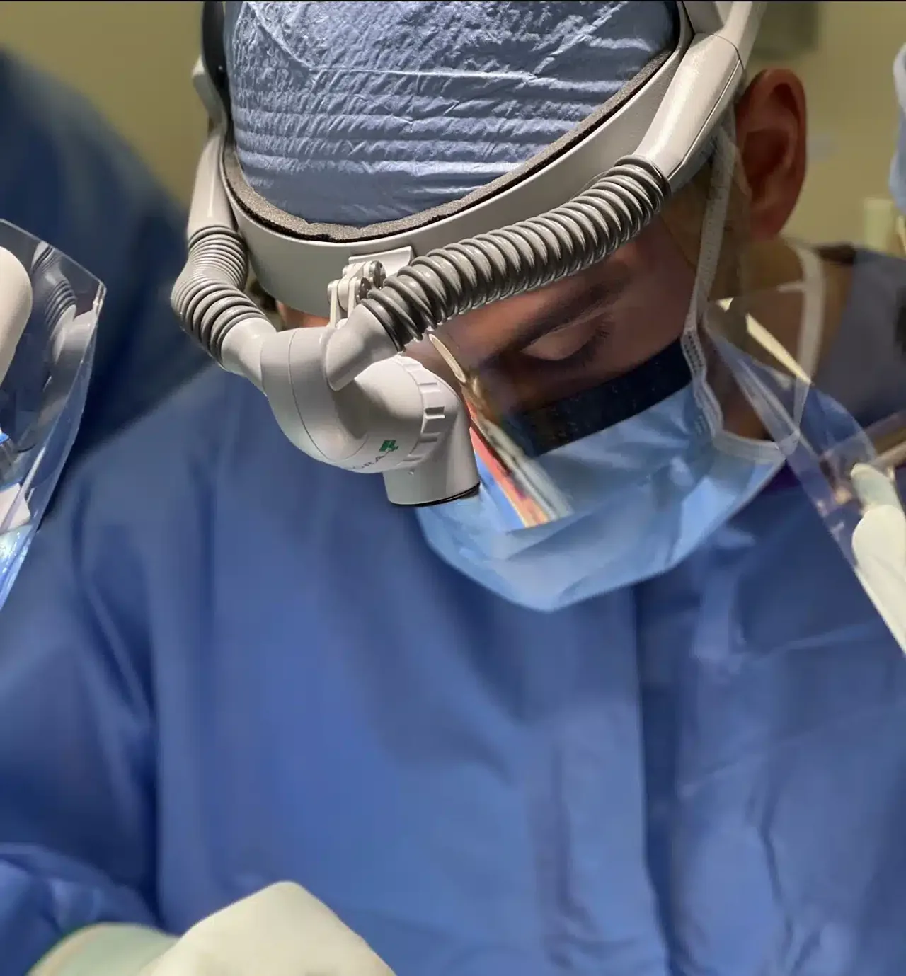 Chad Curtis, DDS, in surgery wearing a gown, mask, face shield, and surgical loupes